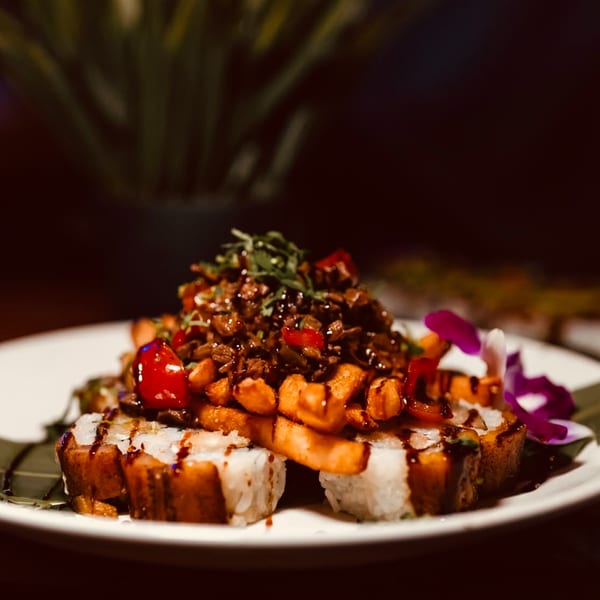 Dominican sushi rolls topped with meat, sweet potato fries, and a purple orchid garnish.