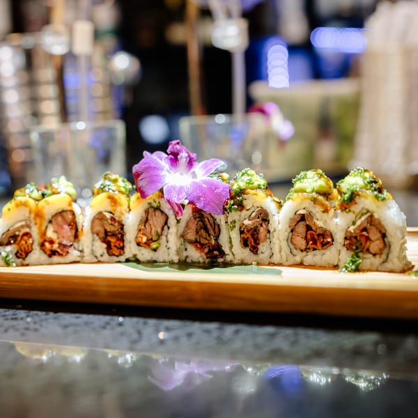 Sushi rolls with beef, avocado, and a purple orchid garnish on a wooden board.