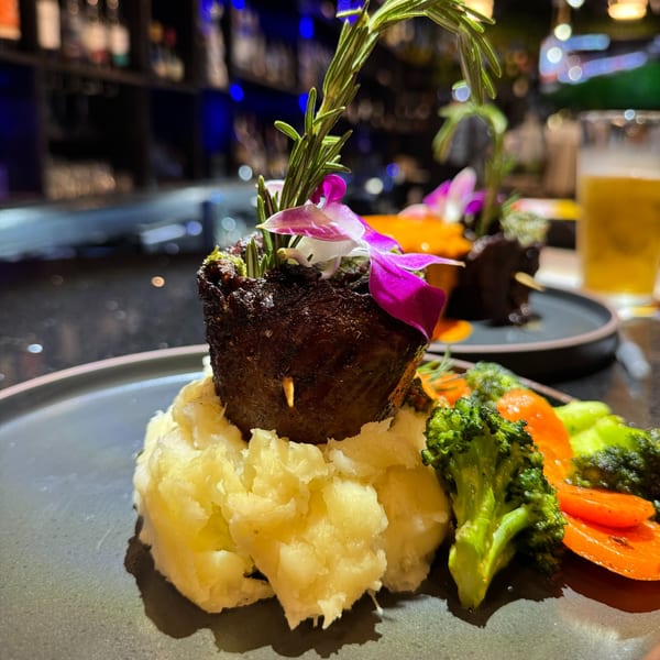 Dominican dish with meat, mashed potatoes, broccoli, and carrots, garnished with rosemary and an orchid.