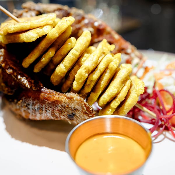 Crispy fried fish with a skewer of golden tostones and a side of dipping sauce.