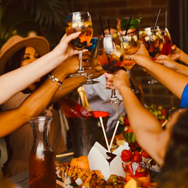 Friends toasting drinks at Eden's Legacy, with a spread of Dominican food and cocktails.