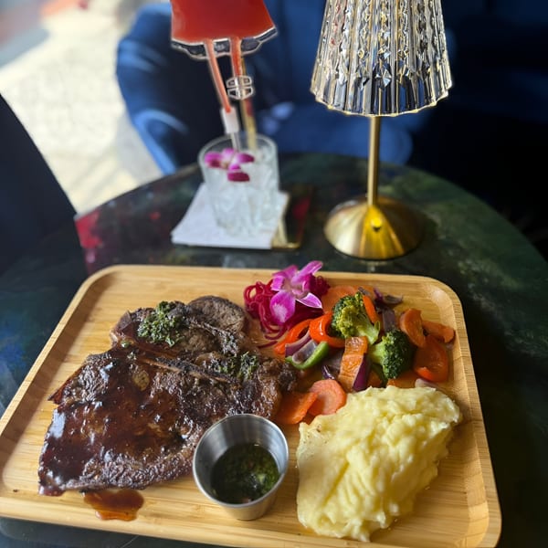 Dominican steak with mashed potatoes, mixed vegetables, and a cocktail on a wooden tray.