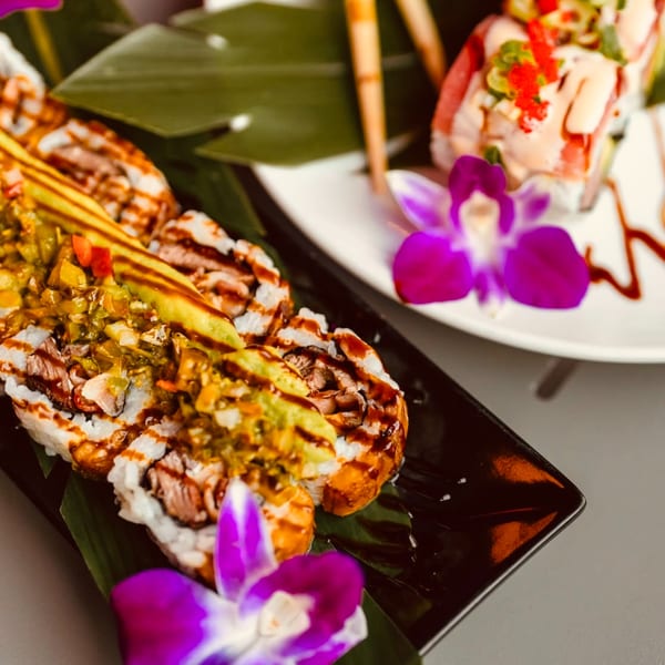 Dominican sushi rolls with meat, avocado, and relish, garnished with purple orchids on a black plate.