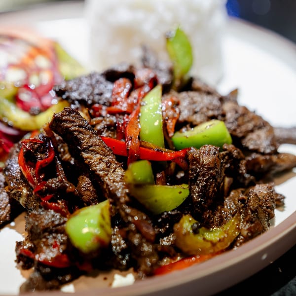 Close-up of Dominican stewed beef with red and green peppers, served with white rice.