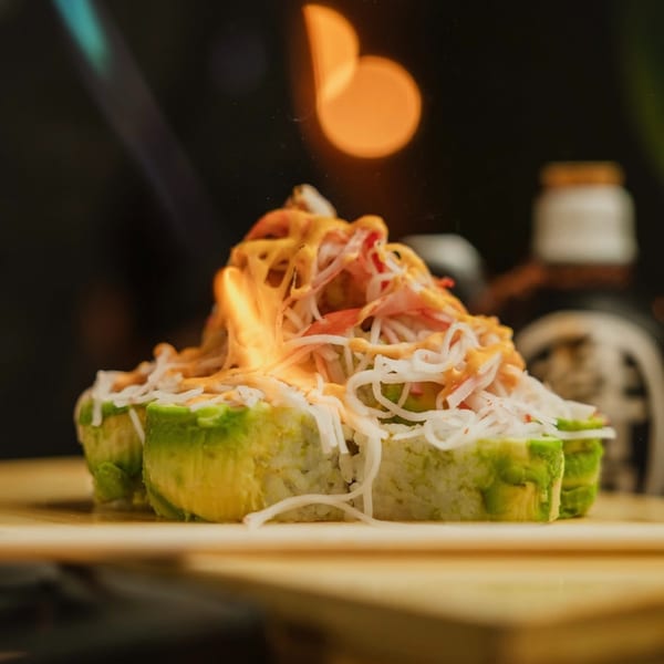 Sushi rolls topped with crab meat, sauce, and a flame, on a wooden board.