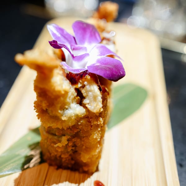 Close-up of a deep-fried Dominican dish, garnished with a purple orchid and served on a wooden board.