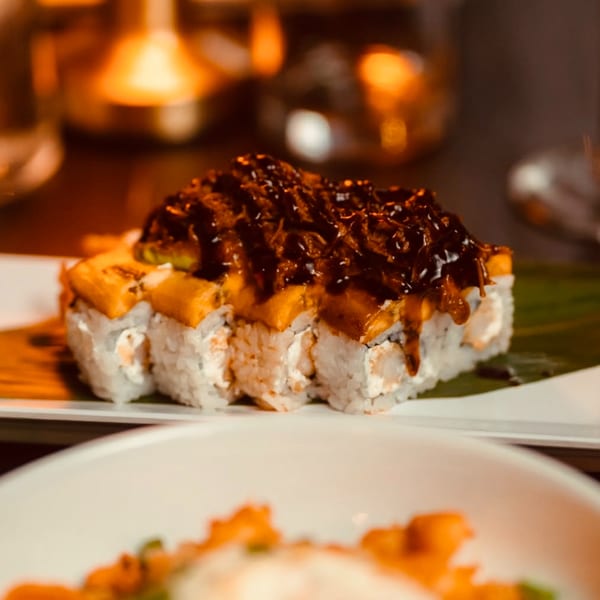 Sushi rolls topped with dark sauce and orange slices, served on a white plate.