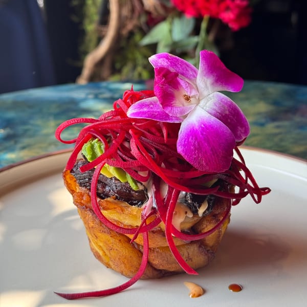 Dominican dish with plantains, meat, red pickled onions, and a purple orchid garnish.