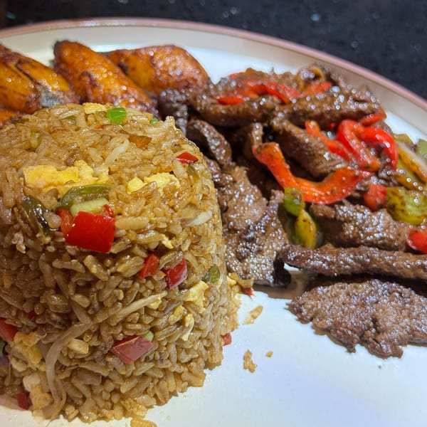 Dominican dish with fried rice, plantains, and seasoned beef strips with peppers on a white plate.