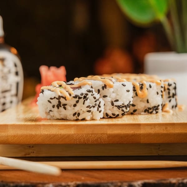 Sushi rolls with black sesame seeds and a creamy sauce on a wooden board with chopsticks.