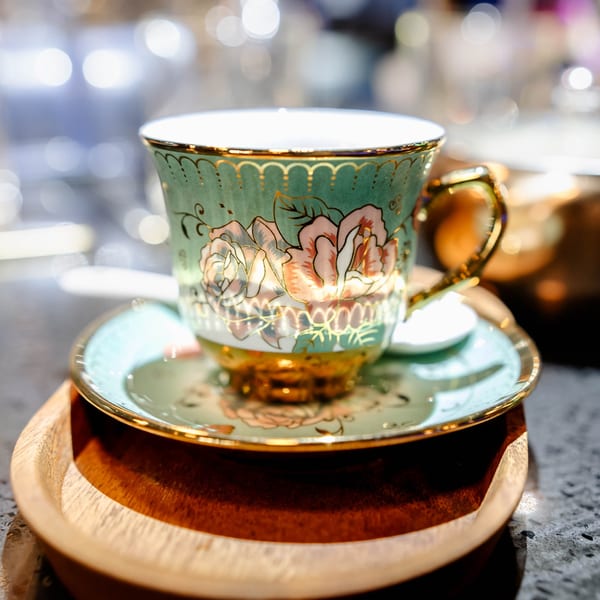 Elegant teal and gold teacup with floral design on a matching saucer and wooden tray.
