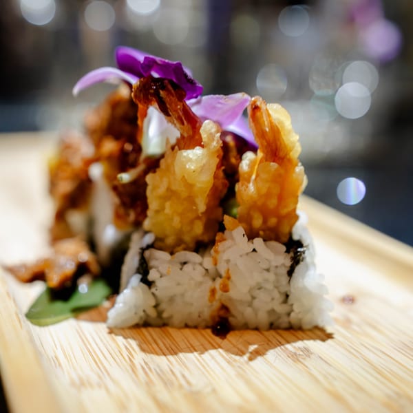 Tempura shrimp sushi rolls with white rice and purple orchid garnish on a wooden board.