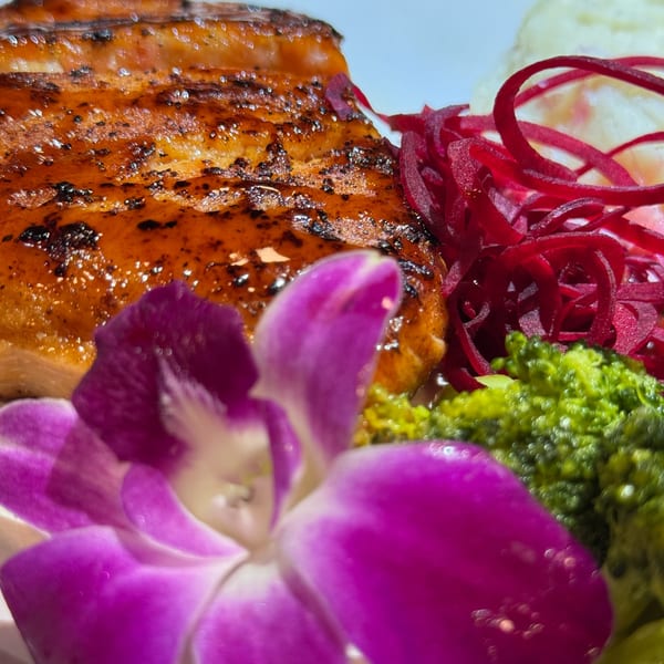 Grilled salmon with glazed skin, shredded red cabbage, broccoli, and a purple orchid garnish.