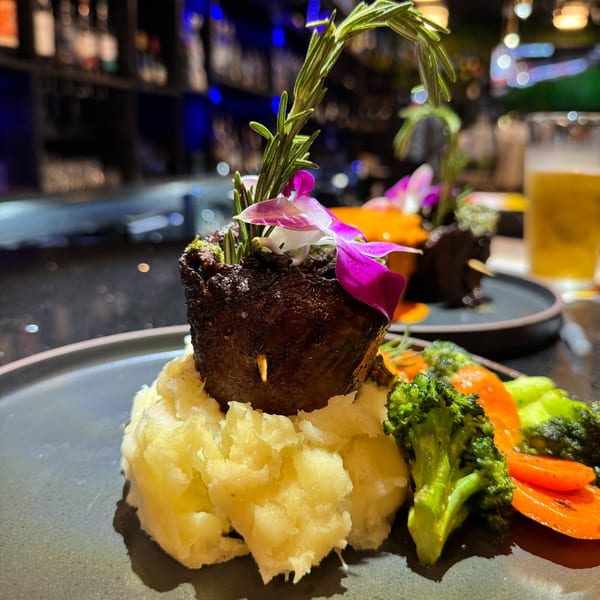 Dominican dish with meat, mashed potatoes, broccoli, and carrots, garnished with rosemary and orchids.