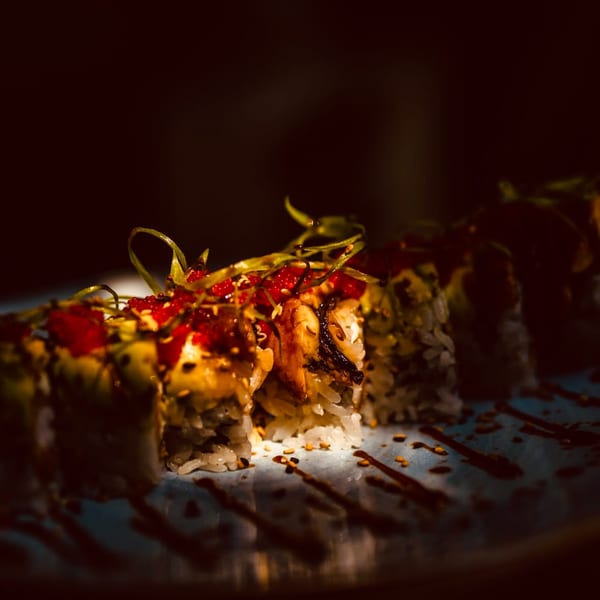 Close-up of sushi rolls topped with red roe, green garnish, and a dark sauce drizzle.